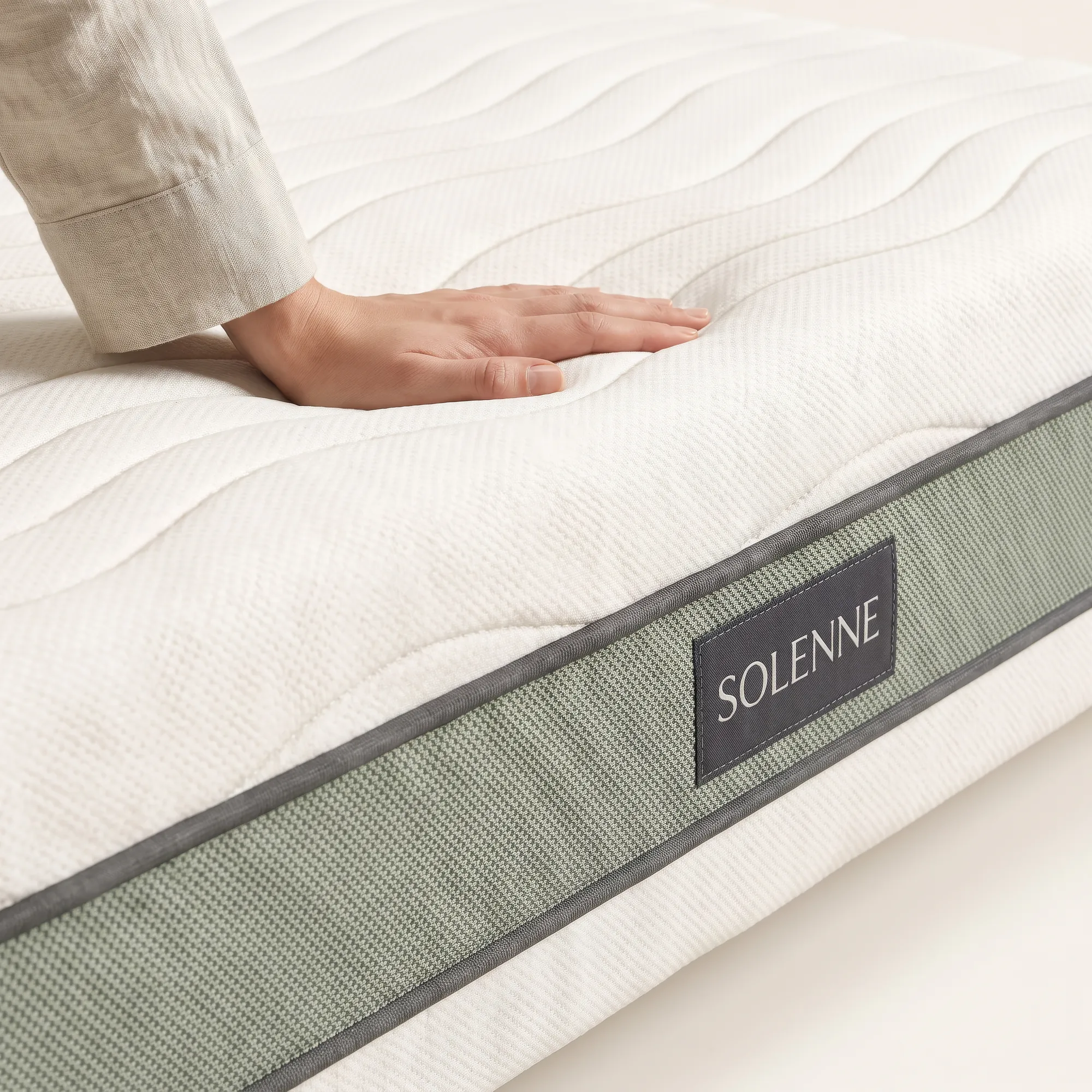Macro of the mattress corner with a hand pressing into the quilted top